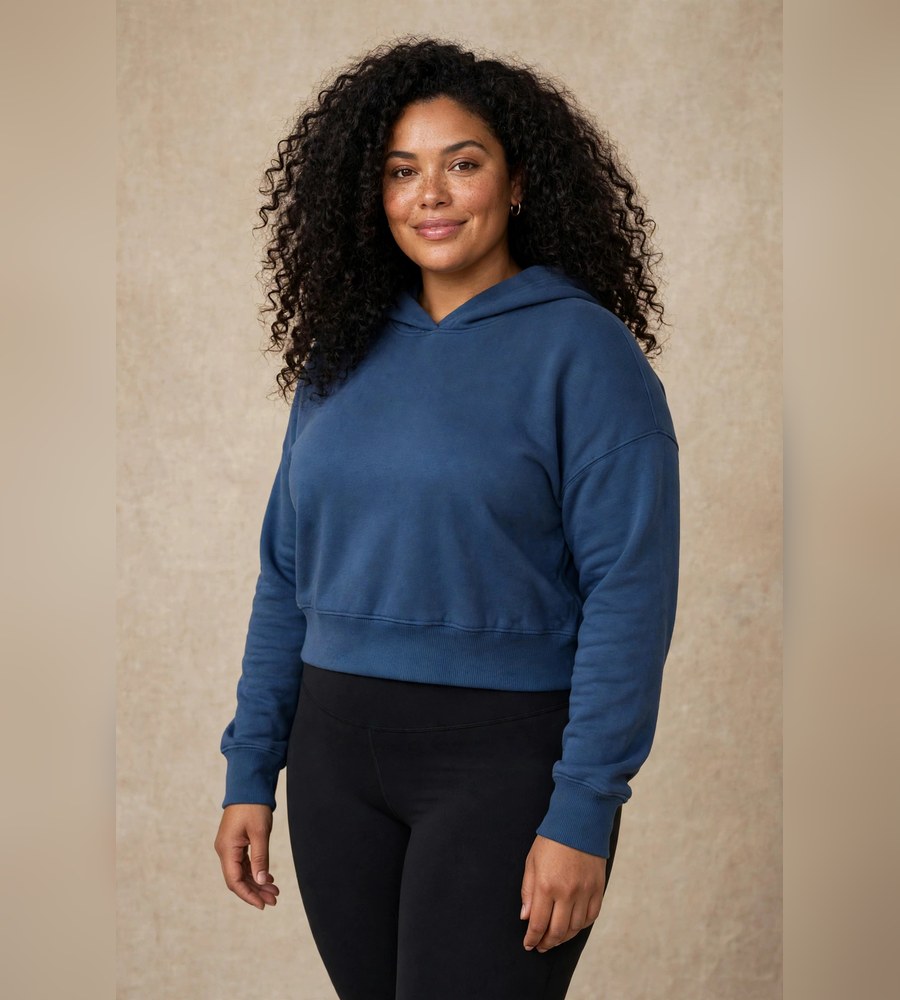 Woman wearing a cropped indigo hoodie, shown with the fused Omega Woman mark and the words EVERY BODY IS A STRONG BODY